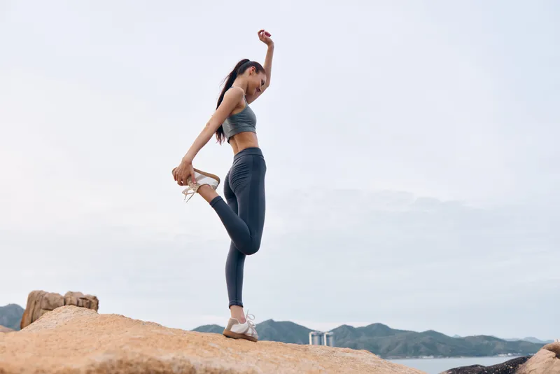 Fit Asian woman stretching on rocks during sunrise in activewear, promoting a healthy lifestyle and fitness concept for exercise and wellness