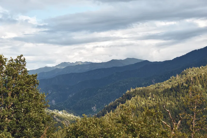 Majestic mountain landscape with rolling hills, dense trees, and a cloudy sky creating a serene outdoor scene rich in natural colors and tranquil atmosphere.