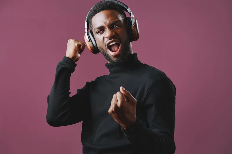 Young African American man enjoying music in stylish headphones, expressing joy and excitement against a vibrant purple background
