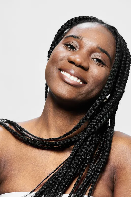 Smiling female model with braided hair, expressing joy and confidence against a clean white background, perfect for beauty and fashion concepts