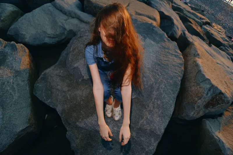 lifestyle woman in modern boho-western denim street style sitting on rocks with film color mood and natural light outdoors