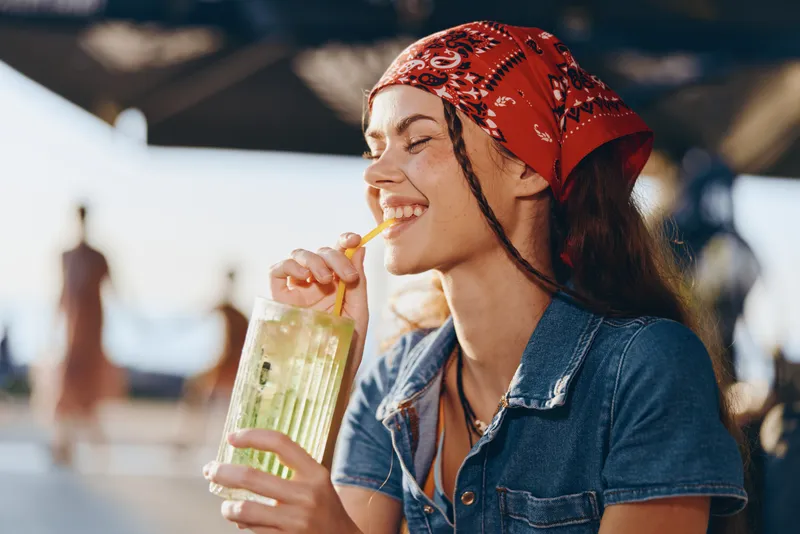 lifestyle woman with red bandana enjoying cold drink outdoors in modern boho-western denim street style with warm film color tones and relaxed summer vibe