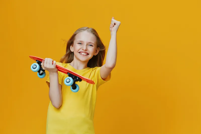 Happy girl celebrating with a skateboard against a bright yellow background, showcasing joy, youthfulness, and a playful lifestyle Perfect for cheerful concepts