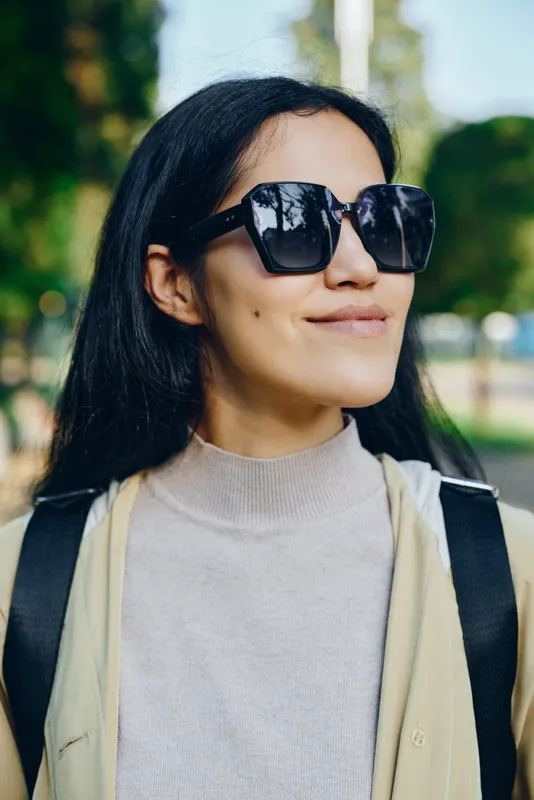 Sunglasses wearing woman outdoors in a park on a sunny day, chic casual attire, calm smile, modern eyewear and confident style captured in natural light