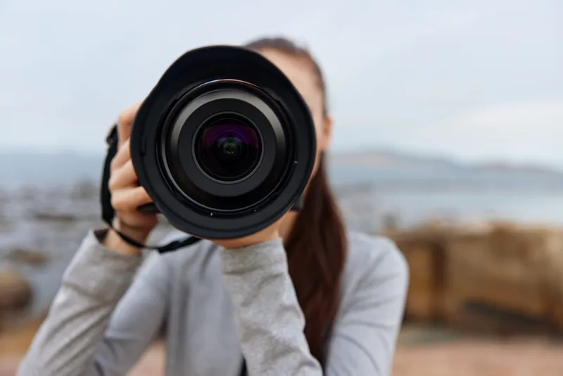 Young female photographer holding a camera, showcasing dedication and artistry amidst a serene outdoor backdrop, exuding creativity and passion for photography