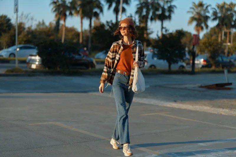 Woman walking casual urban golden smile in parking lot during golden hour glow, candid lifestyle portrait showing authenticity, mindful living and warm emotional storytelling mood.