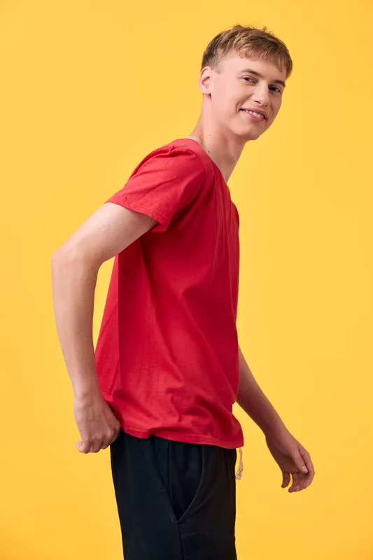 Teen boy in red shirt poses against a bright yellow background, casual and energetic, showcasing youth confidence and a friendly smile.