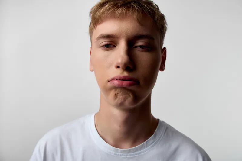 Pouty boy in white shirt makes a playful grimace, closeup shot highlighting facial expression, mood, studio lighting and a neutral, minimal background