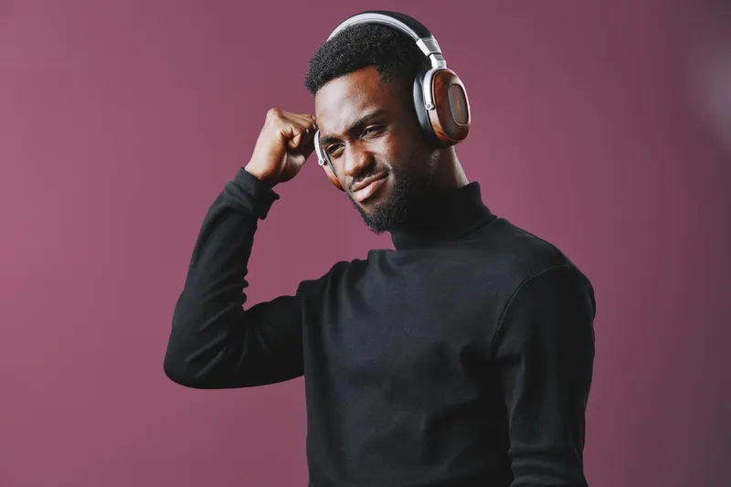 Stylish Black man enjoying music with headphones, displaying confidence and emotion against a vibrant purple background, perfect for modern lifestyle concepts