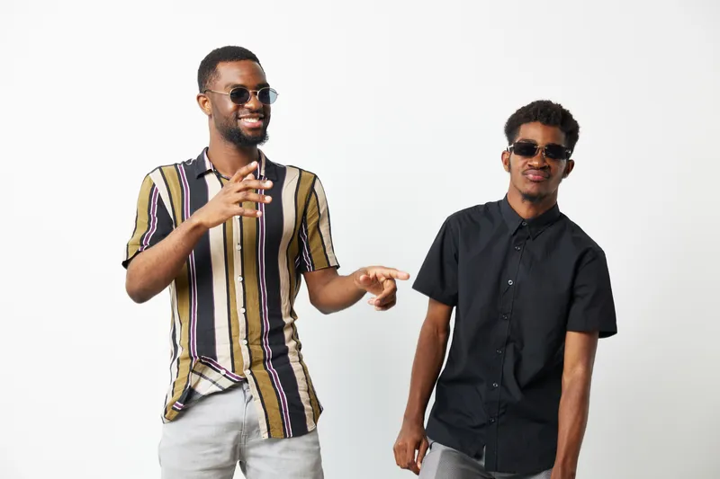 Two smiling black men enjoying a friendly moment, wearing sunglasses and stylish clothes, radiating positivity and happiness in a casual setting.