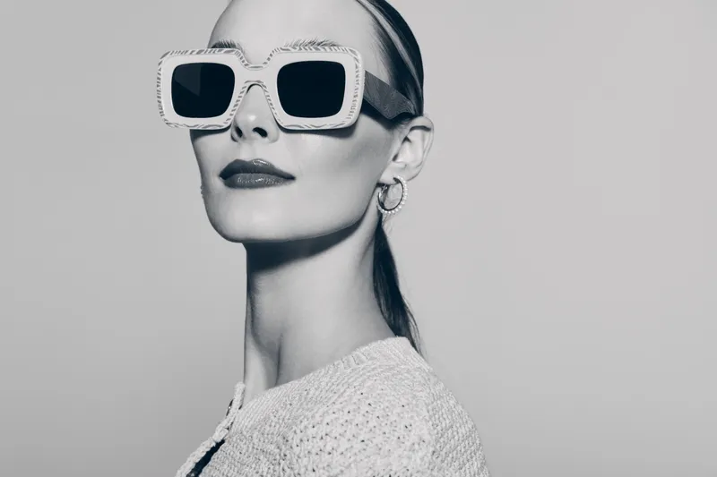Portrait of a confident white woman wearing large square sunglasses and hoop earrings. She is dressed in a textured sweater with sleek hair pulled back. Fashion and style concept.