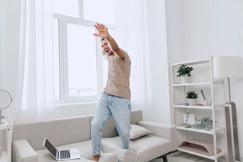 Happy man dancing in a cozy living room, embracing a digital detox while juggling work-life blur and focusing on mental well-being.