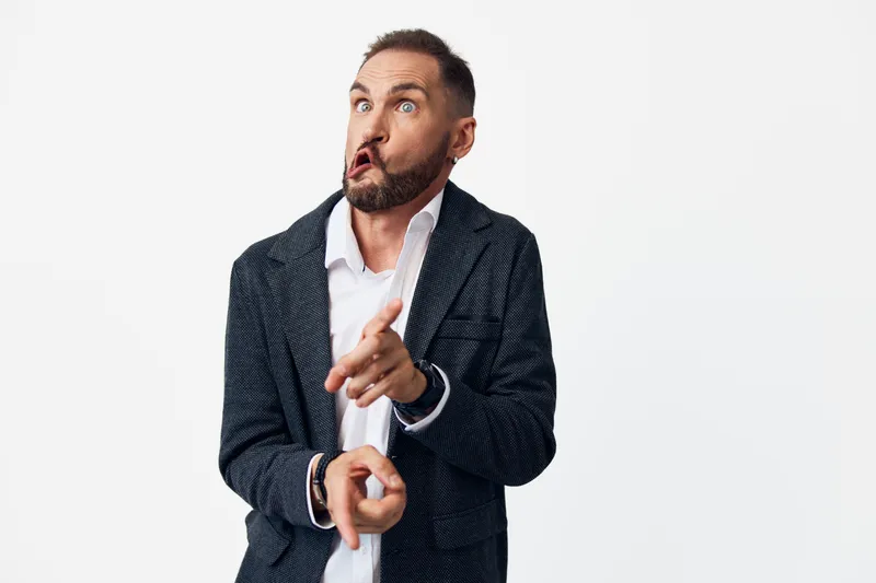 A confident business professional man stands on an isolated colored background, projecting surprise and engagement as he points forward with a dynamic, energetic pose.