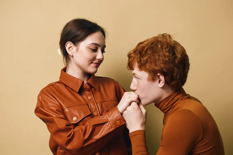 Couple, woman and man in casual clothes with red hair showing affection and intimate moment on beige background. Young people or lovers in warm tones for relationship and care.
