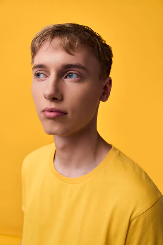 Young man in a yellow shirt against a bright yellow backdrop, looking away with a thoughtful, clean mood suitable for lifestyle and fashion concepts
