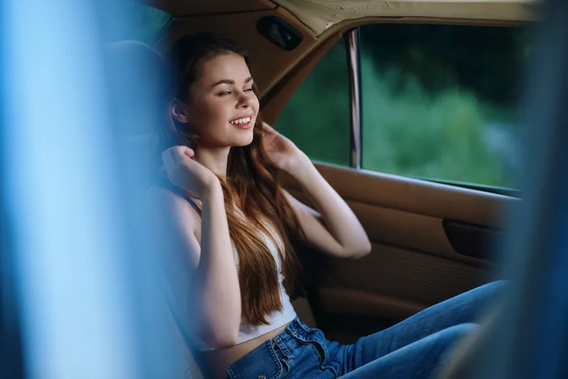 Young woman enjoying music in a vintage car, smiling with closed eyes. Bright atmosphere reflects joy and freedom, emphasizing a relaxed, summery vibe.