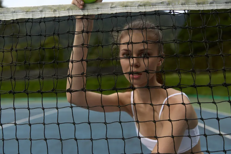 Young female tennis player in a white sports outfit holding a tennis ball, displaying focus and determination on a blue outdoor court