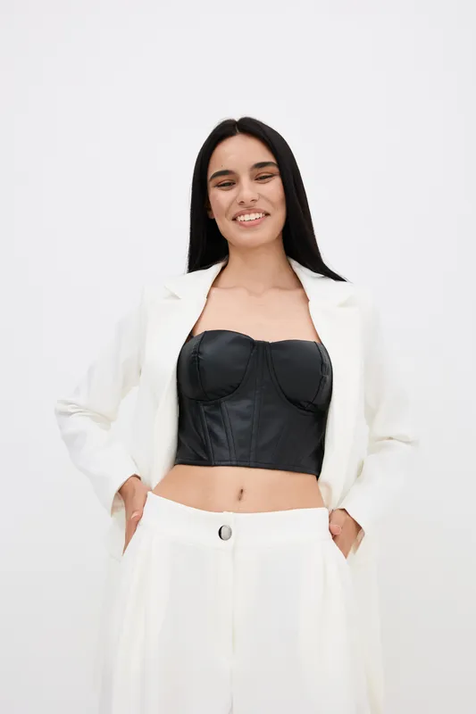 smiling woman in stylish white suit and black leather top posing happily against white background, modern fashion, confident mood, minimalistic studio lighting