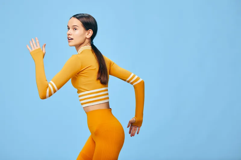 Woman in vibrant orange athletic wear mid movement in a studio, showcasing fitness and sport energy, dynamic pose for training and exercise in a modern, colorful setting.