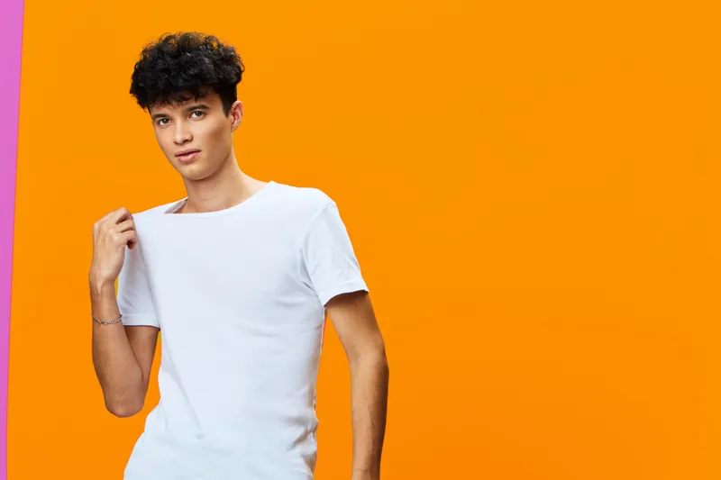 young man in white t-shirt posing against vibrant orange background with relaxed expression and casual hairstyle, bright warm colors enhancing modern studio portrait