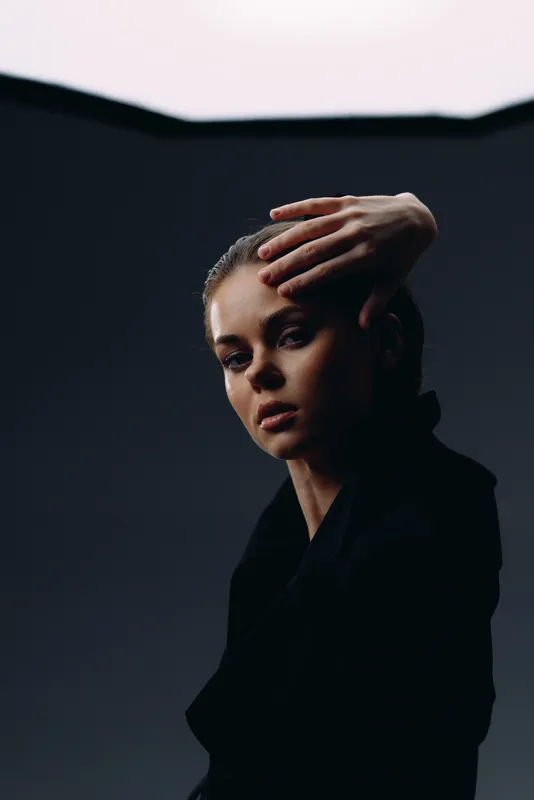 Portrait of a thoughtful woman with hand near face in dark studio lighting, artistic and moody atmosphere