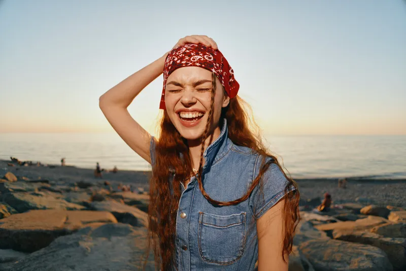lifestyle woman wearing modern boho-western denim street style laughing by the beach in warm natural film color lighting, carefree summer vibe