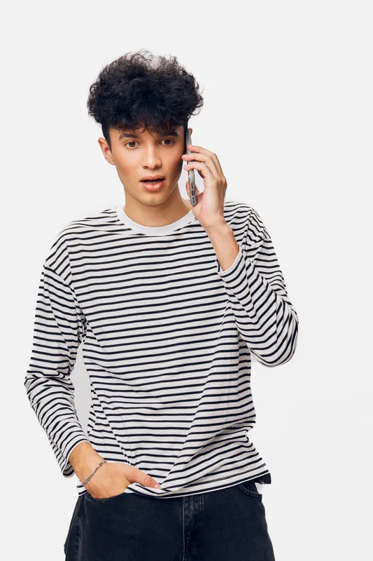Young man talking on smartphone with surprised expression wearing casual striped long-sleeve shirt against plain white background.