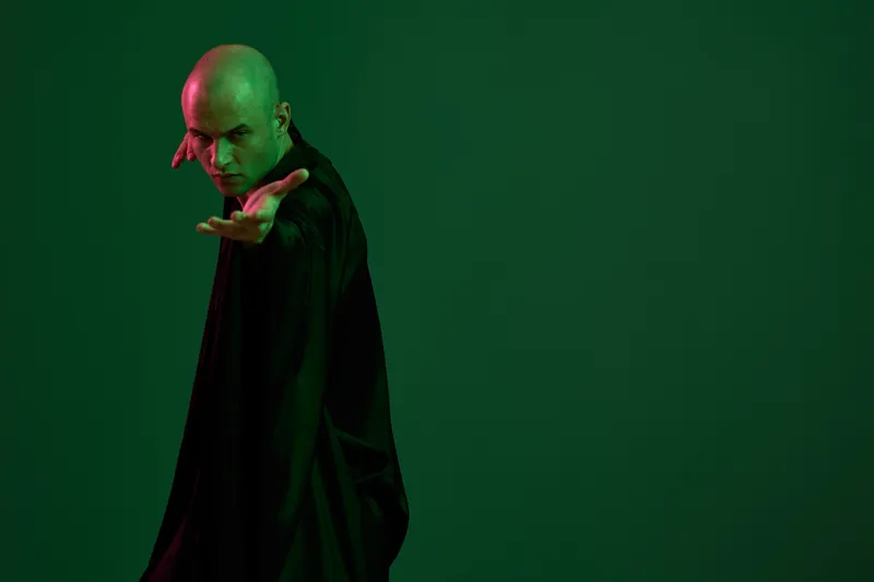 Mysterious man in black attire extending his arm, set against a vivid green background. The image conveys an aura of intrigue and suspense.