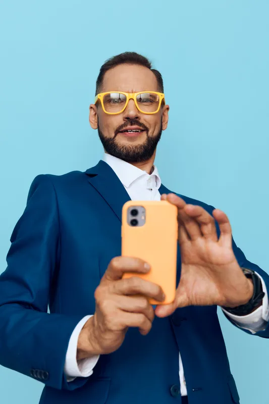 A professional man in a blue suit on a vivid isolated background, smiling with confidence while taking a selfie, conveying focus, motivation, and readiness for business tasks.