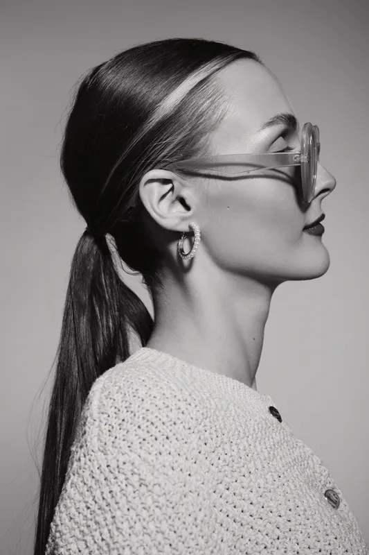 Profile of a young caucasian woman with pale skin wearing glasses and hoop earrings in a knitted sweater. Minimalist black and white portrait.
