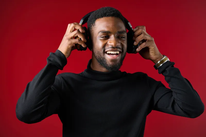 Happy young man enjoying music with headphones against a vibrant red background, showcasing joy, relaxation, and musical passion