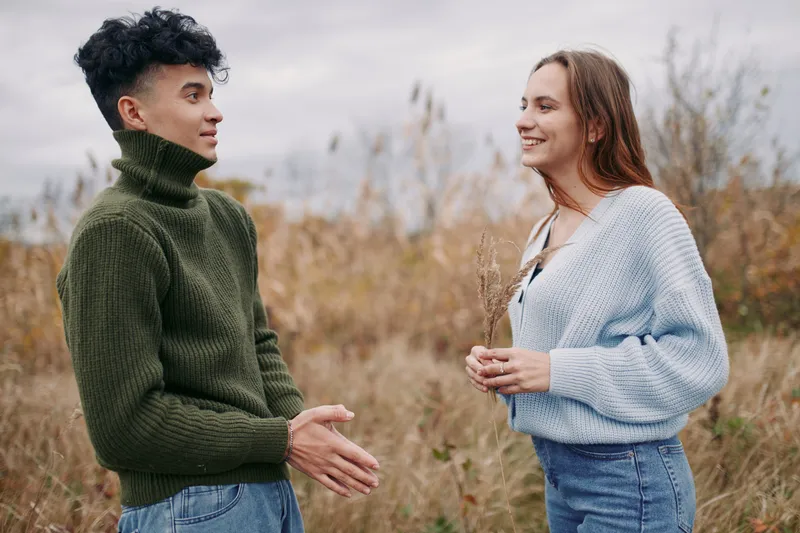 A candid outdoor portrait of two young adults sharing a sincere conversation in a wild meadow, highlighting authentic connection, natural expressions and genuine interaction in soft autumn light.