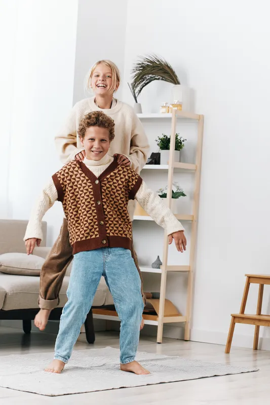 Bright scene capturing a smiling grandmother and grandson dancing indoors in a cozy living room, knit sweaters, warm light, candid family moment, movement and joy.