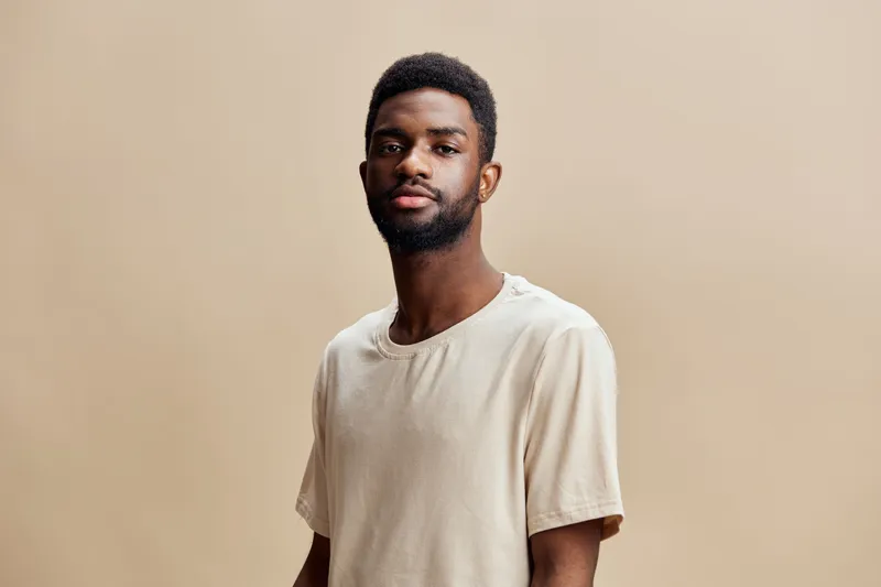 Portrait of a young African male model in a casual beige t shirt against a neutral background, exuding confidence and calmness KEY portrait, male, African, model, confident, casual, beige, t shirt,