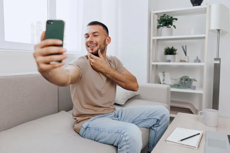 Cheerful man taking a selfie in a cozy living room, showcasing a relaxed and modern atmosphere with soft colors and natural light.