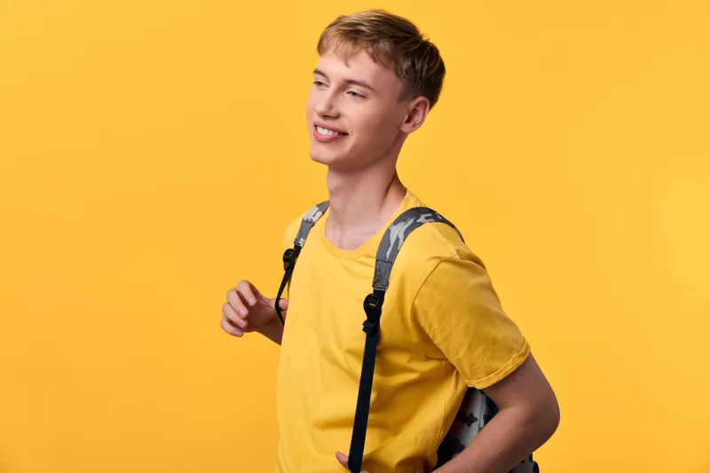 Smiling youth in a bright yellow t shirt with a backpack against a vibrant backdrop, conveying casual style, readiness for school, travel, and everyday adventures.