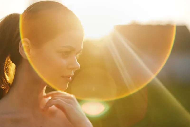 Young woman enjoying a sunny evening, with sunlight illuminating her face, showcasing warmth, beauty, and serenity in a natural setting