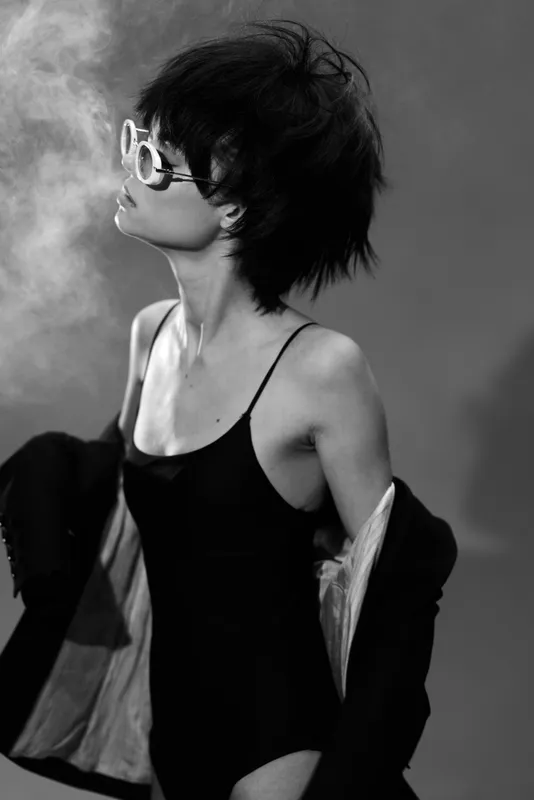 elegant woman with sunglasses and smoke wearing black outfit in black and white