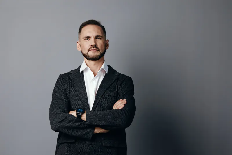 A confident businessman stands with arms crossed against a solid colored isolated background, projecting professionalism, focus, and calm emotion in a modern studio setting.