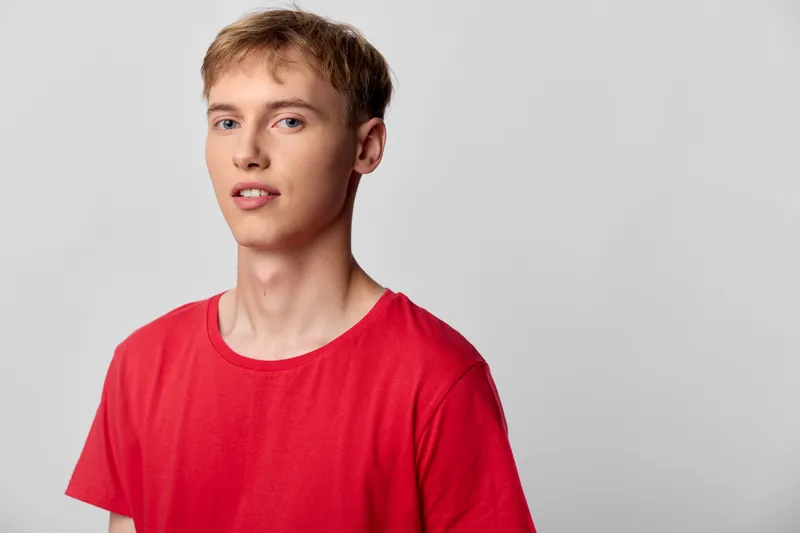Young man in a red shirt stands against a neutral background, a casual studio shot showcasing simple pose and youthful fashion for stock use, clean lighting and modern everyday style