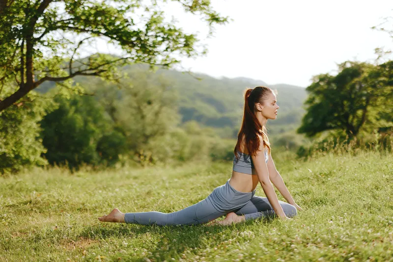 Serene young woman practicing yoga outdoors in a lush green field, showcasing flexibility and tranquility in a natural setting