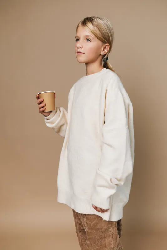 Authentic lifestyle portrait of a young girl in a cozy sweater, holding a cup, capturing a candid school day moment and simple, everyday comfort.
