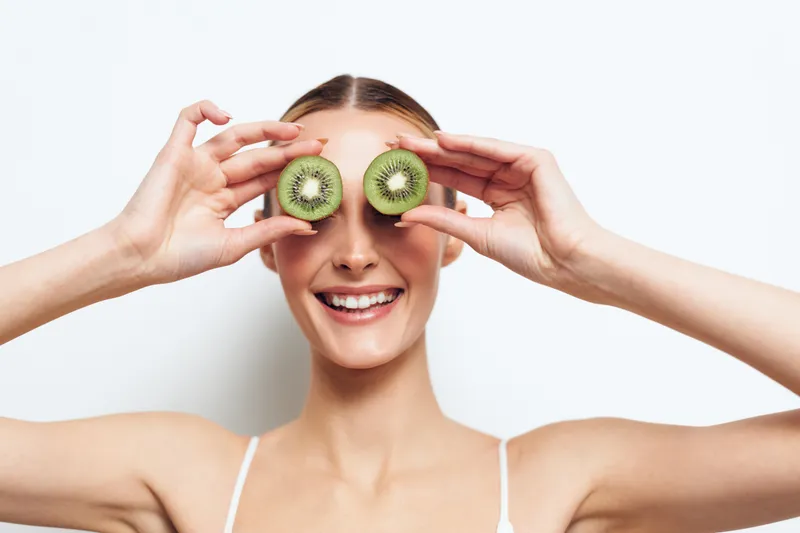 Woman kiwi fruit fresh healthy smiling eyes hands playful wellness concept, young woman holds kiwi halves over eyes on white studio background, showing healthy eating and joy