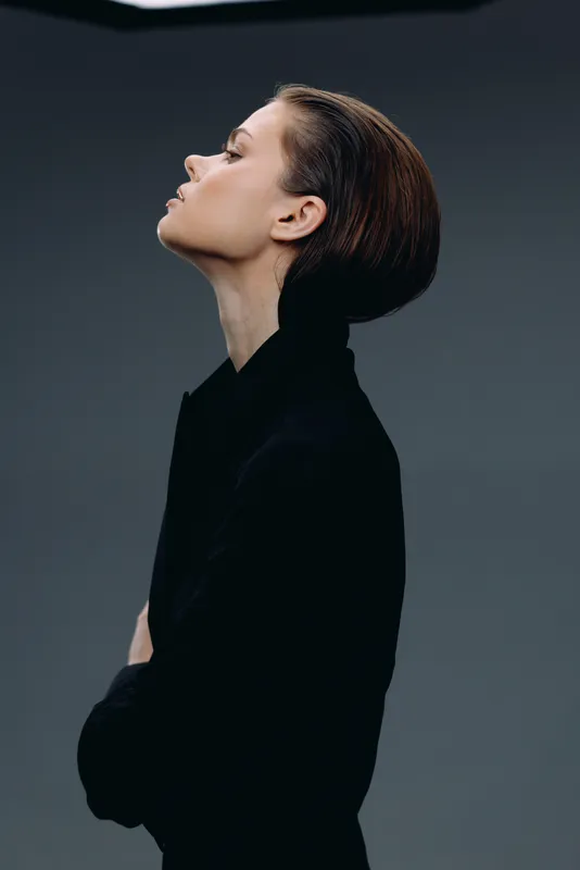 profile of a woman in black turtleneck with short hair against dark background, elegant, thoughtful