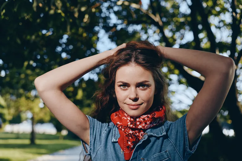 Lifestyle woman in modern boho-western denim street style outdoors, wearing a red bandana, enjoying natural light and film color tones on a sunny day.