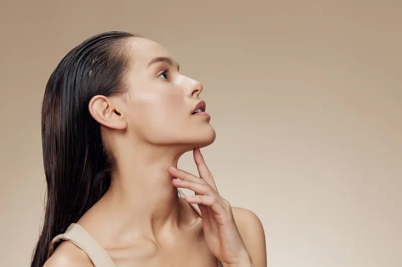 Profile of a young woman with wet hair, showcasing natural beauty and serene expression against a warm beige background Emphasizing healthy skincare and minimalistic style