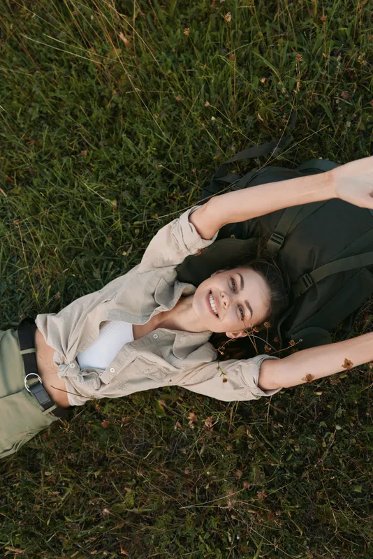 Relaxed woman lying in tall grass, arms stretched above her head, enjoying a carefree outdoor moment. Natural light creates a warm, peaceful mood and wellness themes.