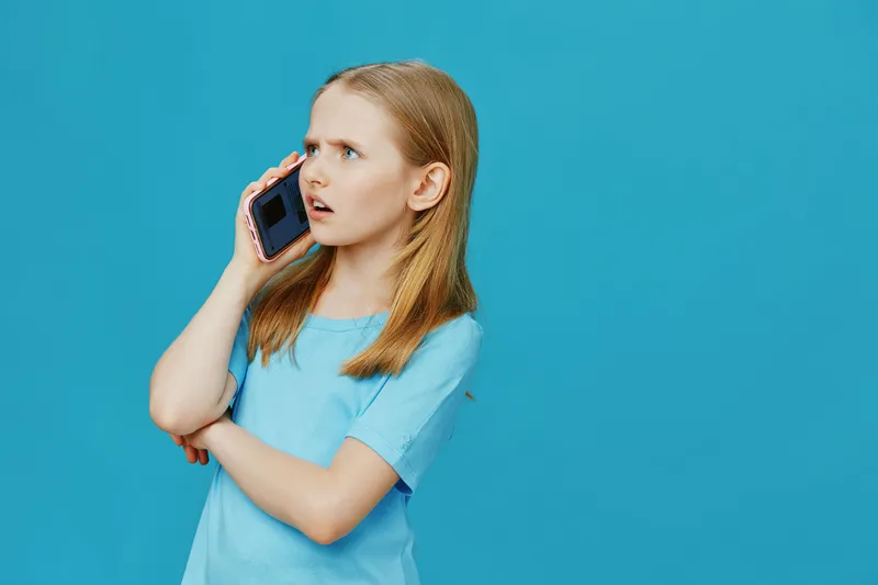 Concerned girl talking on the phone against a blue background, showcasing emotions of surprise and curiosity in a casual blue shirt