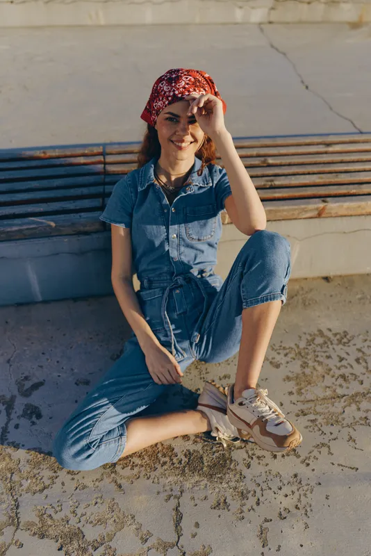Lifestyle woman in modern boho-western denim street style poses outdoors with a red bandana and sneakers, capturing relaxed film color tones and casual fashion attitude.