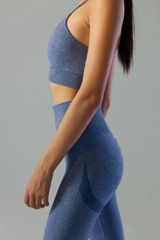 Fit woman sport fitness wearing seamless blue activewear, showing toned body and natural posture with smooth skin and long dark hair against plain background.